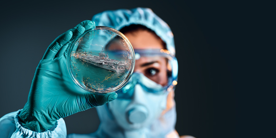 person in personal protective equipment holding a petri dish with an image of a ship on it