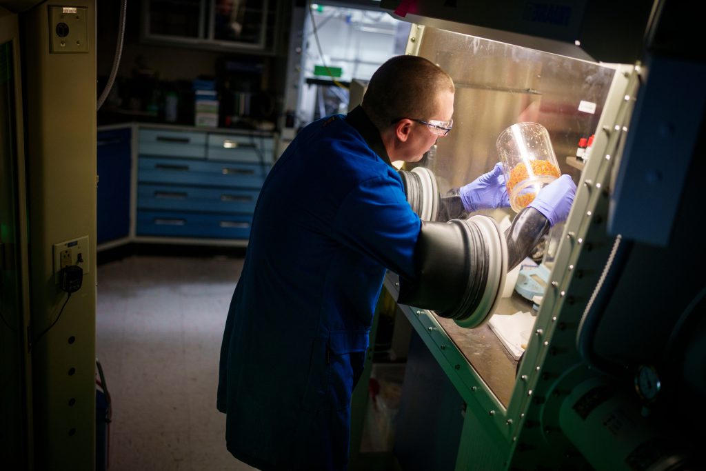 materials chemist works in a glove box, preparing a container filled with bead bits that will turn brown if someone attempts to tamper with the container’s contents
