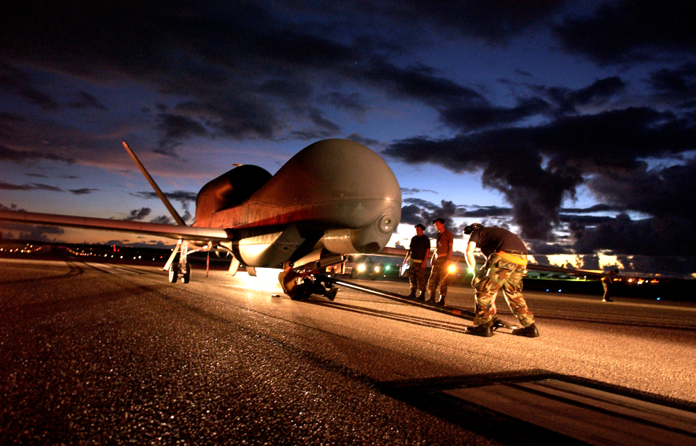 Image of several Department of Defense personnel inspecting an unmanned aircraft on a runway.