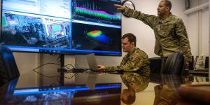 USAF techs discuss electromagnetic spectrum operations at computer monitors.